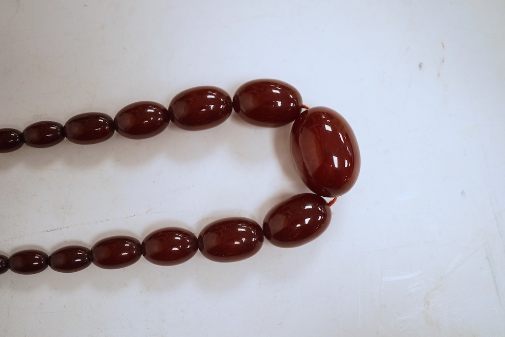 A single strand graduated oval simulated amber bead necklace, 72cm, gross weight 64 grams, together with a simulated cherry amber bracelet.
